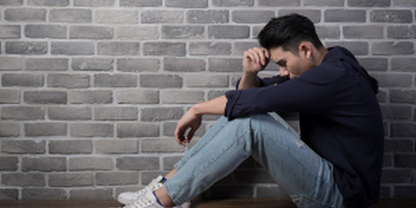 Man sitting with head on hands in front of brick wall